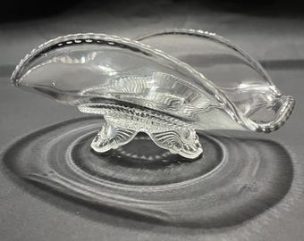 May include: A clear glass bowl with a scalloped edge and a decorative base. The bowl is shaped like a shell and has a delicate, feminine design.