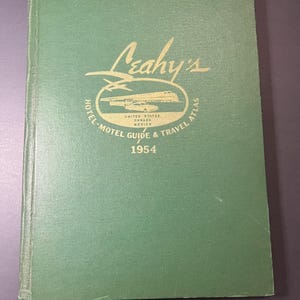 May include: A vintage green "Leahy's Hotel-Motel Guide & Travel Atlas" from 1954. The cover features gold lettering and an illustration of a car and plane. The atlas covers the United States, Canada, and Mexico.