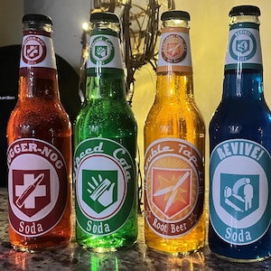 Peut inclure: Quatre bouteilles de soda en verre avec des liquides et des étiquettes de couleurs différentes. Les étiquettes présentent un bouclier blanc avec une icône et un texte différents sur chacune. Les étiquettes indiquent "Jugger-Nog Soda", "Speed Cola Soda", "Double Tap Root Beer", et "Revive! Soda".
