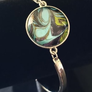 May include: Silver bracelet with a round, blue, green, black, and gold marbled design charm.