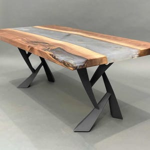 May include: A rectangular wooden table with a clear epoxy resin center. The table has a natural wood grain finish and sits on black metal legs. The table is approximately 72 inches long.
