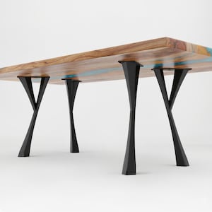 May include: A rectangular wooden table with a natural wood grain finish and blue resin accents. The table is supported by four black, geometric-shaped metal legs. The table's dimensions are not visible in the image.