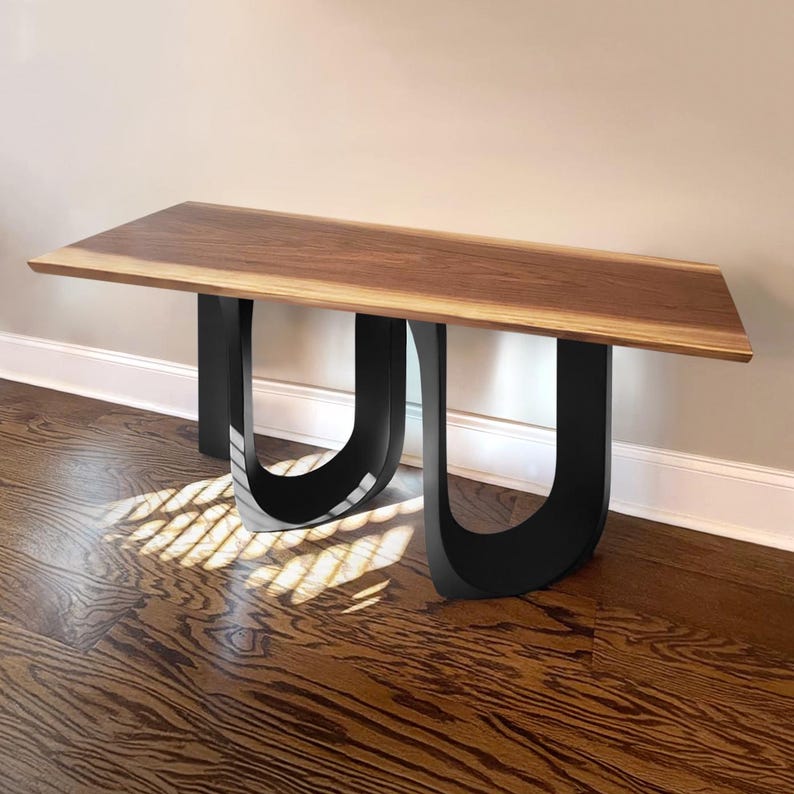 May include: A modern wooden bench with a rectangular top and U-shaped black legs. The tabletop is a warm brown color, and the legs are a glossy black. The bench is placed against a neutral wall and hardwood floor.