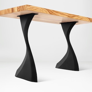 May include: A wooden table with a light brown, textured surface. The table is supported by two black, sculptural legs. The legs have a curved, hourglass-like design, adding a modern aesthetic to the furniture.
