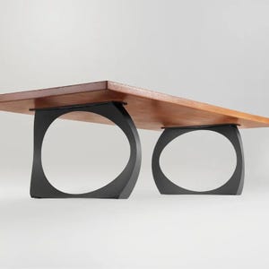 May include: A wooden table with two black metal legs. The legs are shaped like a circle with a curved edge.
