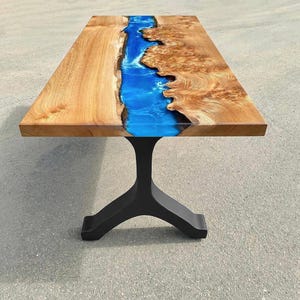 May include: A wooden table with a blue epoxy resin river running down the center. The table has a black metal base with a tripod design.