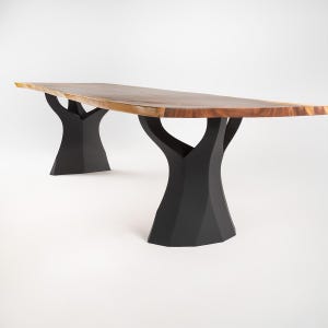 K&ouml;nnte beinhalten: Ein gro&szlig;er, rechteckiger Holztisch mit nat&uuml;rlicher Holzmaserung. Der Tisch wird von zwei schwarzen, baumf&ouml;rmigen Untergestellen getragen. Der Tisch ist ca. 274 cm lang und 102 cm breit.