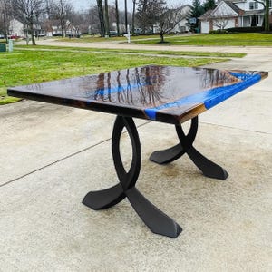 May include: A rectangular wooden table with a glossy, dark brown surface and blue resin accents. The table is supported by black, curved metal legs. The table measures approximately 152 cm long and 76 cm wide.