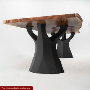 K&ouml;nnte beinhalten: Ein Holztisch mit einer Tischplatte aus nat&uuml;rlichem Holzmaserung und schwarzen baumf&ouml;rmigen Beinen. Der Tisch hat eine rechteckige Form mit einer rohen Kante auf einer Seite. Die Beine sind aus schwarzem Metall und bieten eine stabile Basis.