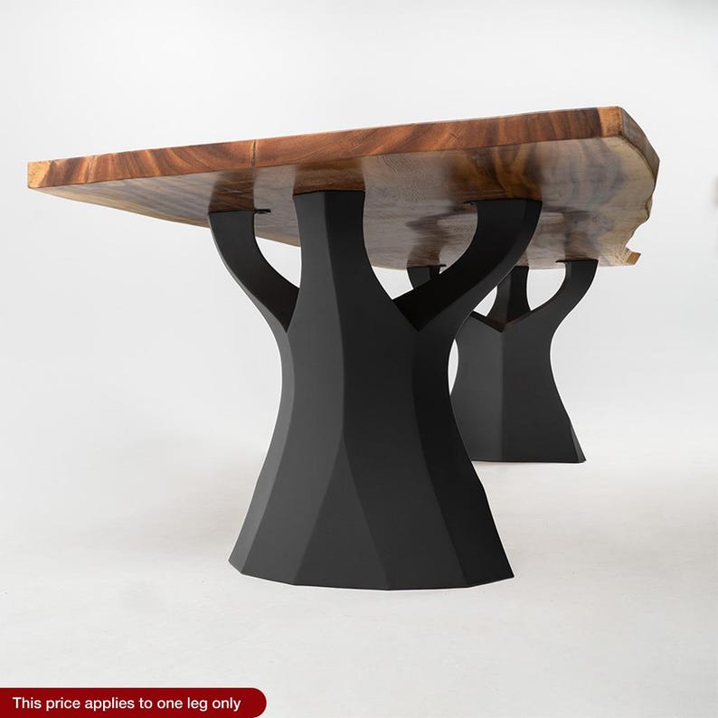 K&ouml;nnte beinhalten: Ein Holztisch mit einer Tischplatte aus nat&uuml;rlichem Holzmaserung und schwarzen baumf&ouml;rmigen Beinen. Der Tisch hat eine rechteckige Form mit einer rohen Kante auf einer Seite. Die Beine sind aus schwarzem Metall und bieten eine stabile Basis.