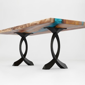 May include: A rectangular wooden table with a live edge and blue resin accents. The table is supported by two black, curved metal legs. The wood has a natural, warm tone, and the resin adds a pop of color.