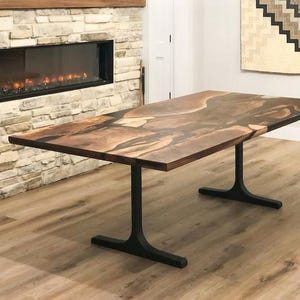 May include: A large, live edge dining table with a natural wood top and black metal legs. The table top has a unique, organic shape and a rich brown color. The legs are simple and sturdy, providing a strong base for the table.