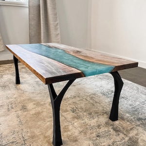 May include: A rectangular coffee table with a wooden top and black metal legs. The tabletop features a river of blue resin flowing between two sections of natural wood. The legs are shaped like tree branches.