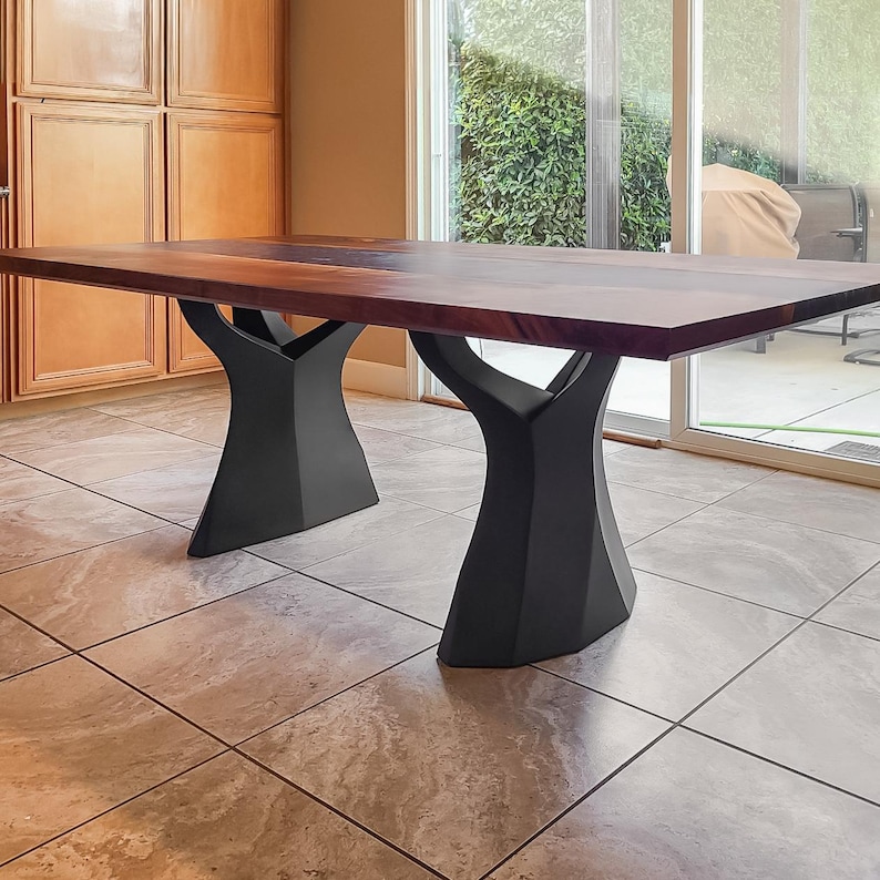 K&ouml;nnte beinhalten: Rechteckiger Esstisch aus Holz mit einer dunkelbraunen Oberfl&auml;che und schwarzen, baumf&ouml;rmigen Beinen. Der Tisch steht auf einem gefliesten Boden. Der Tisch ist etwa 240 cm lang.