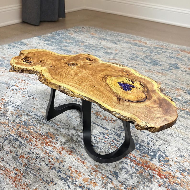 May include: A live edge coffee table with a natural wood grain top and a black metal base. The table's top is approximately 48 inches long and features a unique, organic shape with a blue resin inlay. The base has a curved, modern design.
