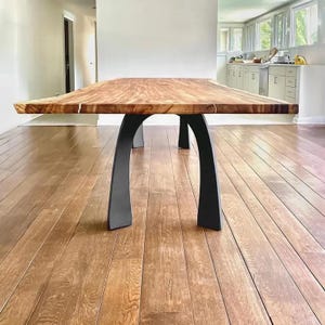 May include: A large wooden dining table with a live edge top and black metal legs. The table is shown in a room with hardwood floors.