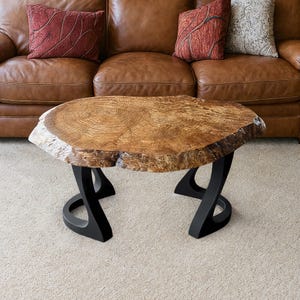 May include: A live edge coffee table with a natural wood grain top. The table is supported by black metal legs. The table's top is approximately 48 inches long and 30 inches wide.