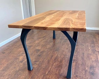 May include: A wooden dining table with a natural wood finish and black metal legs. The legs are curved and have a unique design.