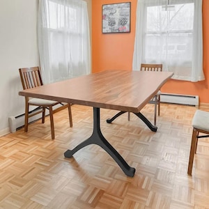 May include: A wooden dining table with a live edge top and black metal legs. The table is in a room with hardwood floors and white curtains.