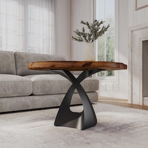 May include: A round wooden coffee table with a natural wood finish and a black metal base. The base is shaped like an X with a curved design.
