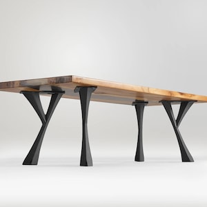 May include: A wooden table with a natural wood top and four black metal legs. The legs are shaped like a Y and have a curved design.