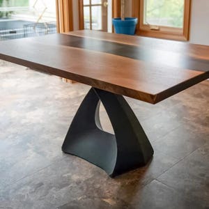 Peut inclure: Une table à manger en bois avec un incrustation en résine époxy noire. La table a un piétement triangulaire unique en métal noir.