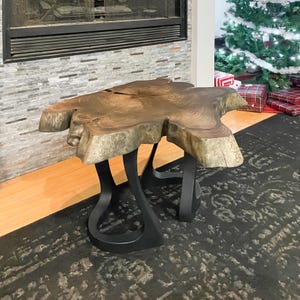 May include: A live edge coffee table with a unique, organic shape. The tabletop is a rich brown with visible wood grain, supported by black, curved metal legs. The table is approximately 48 inches long and 30 inches wide.