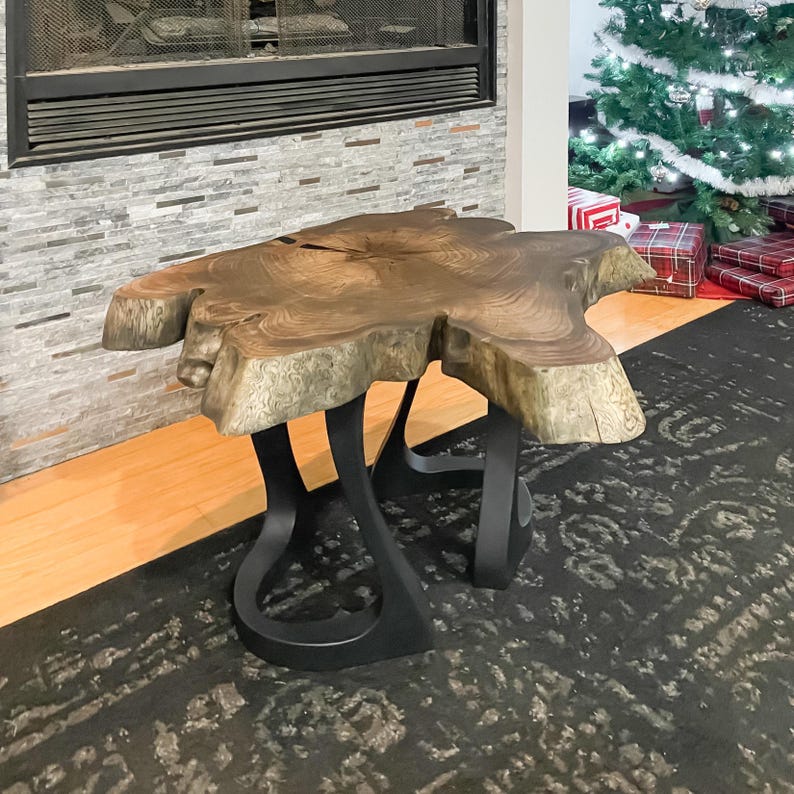 May include: A live edge coffee table with a unique, organic shape. The tabletop is a rich brown with visible wood grain, supported by black, curved metal legs. The table is approximately 48 inches long and 30 inches wide.