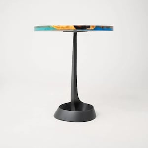 May include: A round side table with a black metal base and a colorful resin tabletop. The tabletop features shades of blue, green, and brown.