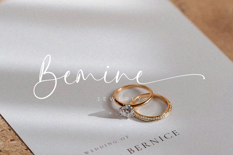 May include: Two gold wedding bands with a single diamond ring on a white card with the text "Bemine Jewelry" and "Wedding of Bernice".