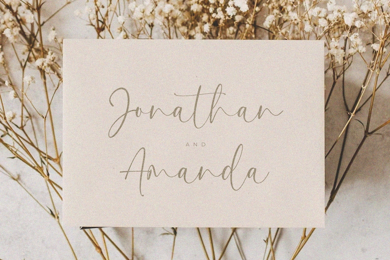 May include: A simple, elegant wedding announcement card with the names "Jonathan and Amanda" written in a cursive script font on a beige background.