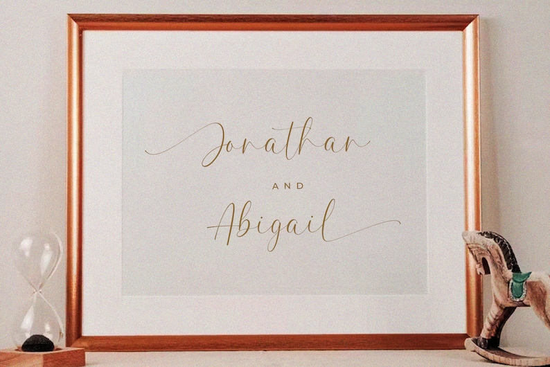 K&ouml;nnte beinhalten: Ein gerahmter Druck mit den Namen "Jonathan" und "Abigail", die in Schreibschrift in goldenen Buchstaben auf wei&szlig;em Hintergrund geschrieben sind.