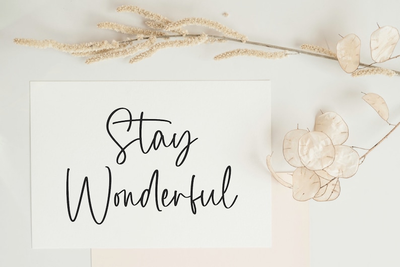 May include: A white card with black calligraphy that reads "Stay Wonderful" on a white background with dried flowers.