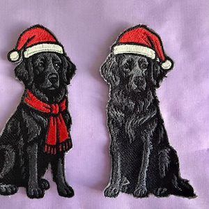 Peut inclure: Deux écussons brodés de chiens noirs portant des bonnets de Père Noël et des écharpes rouges. Les chiens sont assis, avec des coutures détaillées montrant leur fourrure et leurs traits. Les écussons sont sur un fond violet clair.
