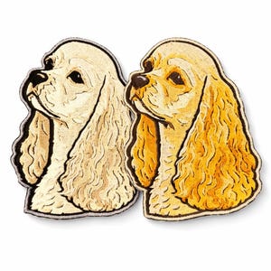 May include: Two embroidered Cocker Spaniel dog head patches. One is cream-colored, the other golden yellow. Both have black outlines and detailed facial features. The patches are designed to be sewn or ironed onto fabric.