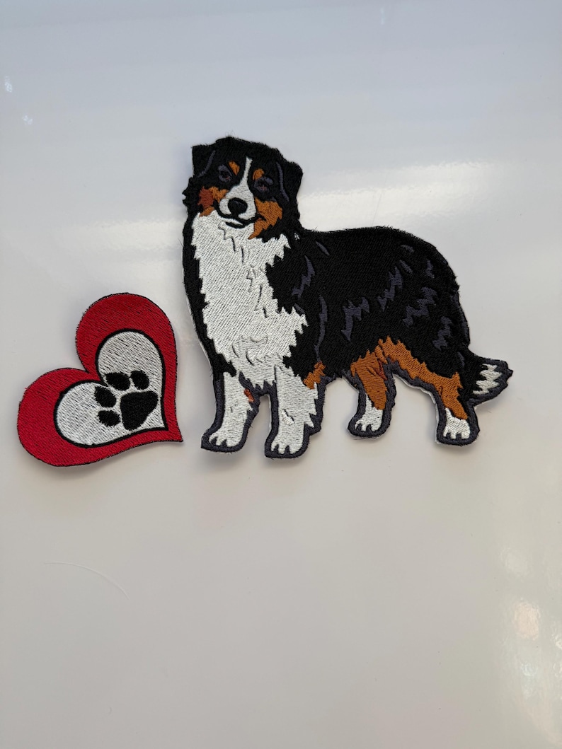May include: Embroidered patch set featuring an Australian Shepherd dog and a red heart with a paw print. The dog patch is black, white, and brown. The heart has a red border and a white center with a black paw print.