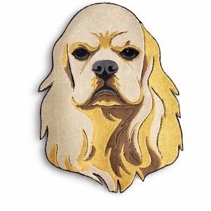 Könnte beinhalten: Gestickter Aufnäher mit dem Kopf eines Cavalier King Charles Spaniel-Hundes. Das Design verwendet cremefarbene, goldene und braune Fäden, um das Fell des Hundes zu erzeugen, mit schwarzen Details für Augen und Nase. Der Aufnäher ist detailliert.