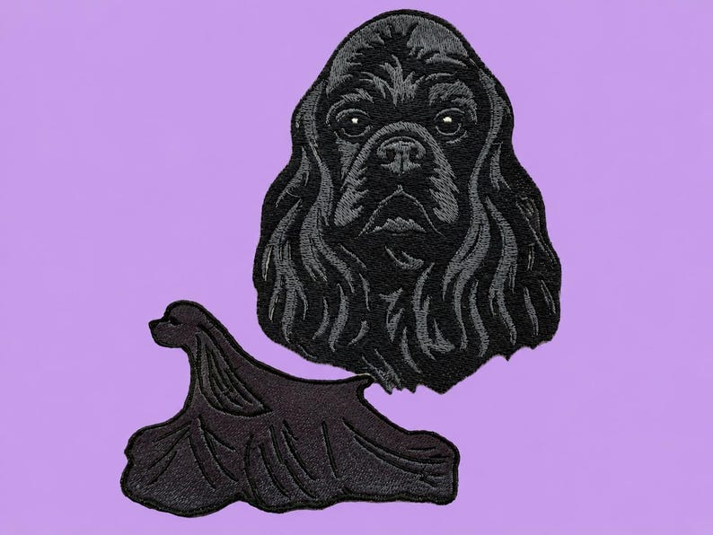 May include: Two black embroidered patches of a Cocker Spaniel dog on a lilac background. One patch is the dog's head, and the other is the dog's body. The patches are detailed with textured stitching, showcasing the dog's fur and features.