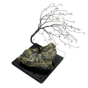 Könnte beinhalten: Eine Drahtskulptur eines Baumes mit einem schwarzen Drahtstamm und Ästen. Der Baum steht auf einem grauen Steinsockel mit einem schwarzen quadratischen Sockel.