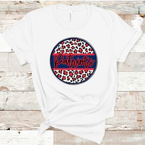 K&ouml;nnte beinhalten: Wei&szlig;es T-Shirt mit einem roten, wei&szlig;en und blauen Kreisdesign. Der Kreis zeigt ein Leopardenmuster und das Wort "Patriots" in rotem Glitzer.