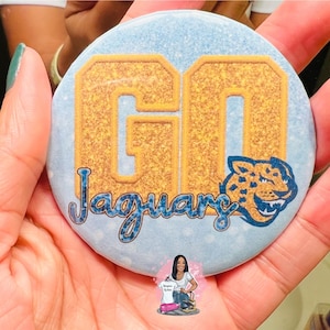 May include: A blue and gold round mirror with the words "GO Jaguars" and a jaguar head graphic.