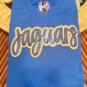 May include: A royal blue sweatshirt with a gold and black sequined "Jaguars" design.