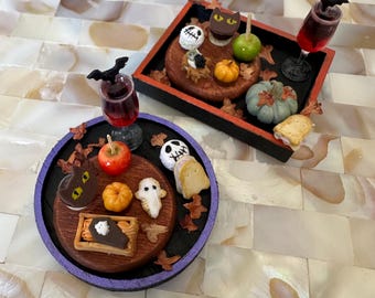 Op de afbeelding: Twee Halloween-charcuterieplanken met een selectie griezelige lekkernijen, waaronder een zwarte kat, een spook, een pompoen en een schedel. De planken zijn versierd met herfstbladeren en een paarse en zwarte rand.