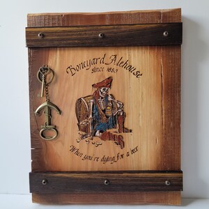 Mancave, entertainment room Wall Keyholder with Hand Painted Pirate Skeleton, paint colors are blue, red, white and gold. Handcrafted with Cedar and Wenge Wood. Comes with brass anchor bottle opener and a small brass key. Measures 13 inches tall.