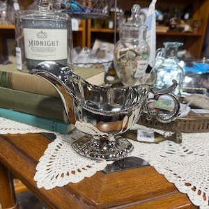 May include: A white ceramic mug with a black handle and the text "But First, Coffee" in a handwritten style. The mug is on a white surface. The mug is approximately 4 inches tall.