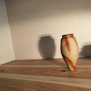 Op de afbeelding: Een keramische vaas met een taps toelopende voet en een brede opening, met een crèmekleurig oppervlak versierd met gedurfde, verticale strepen van roodbruin glazuur die in een vloeiend, organisch patroon rond het lichaam van de vaas lopen.