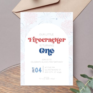 Peut inclure: Une invitation blanche avec un motif de feux d'artifice bleus et rouges. Le texte indique "Notre petit pétard a un an." L'invitation comprend les détails d'une fête de premier anniversaire, y compris la date, l'heure et l'adresse. Les informations de RSVP sont également incluses.