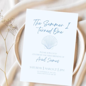 Puede incluir: Una tarjeta de invitación azul claro con el texto "The Summer I Turned One" y un gráfico de concha. La tarjeta también incluye el nombre "Ariel James" y los detalles del evento.