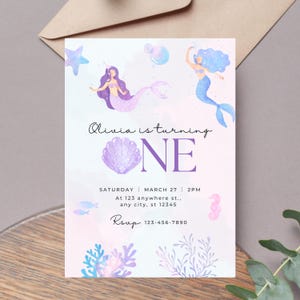 May include: A mermaid-themed birthday invitation with watercolour illustrations. The invitation features two mermaids, a seashell, and aquatic elements. Text includes the name "Olivia", the number "ONE", date, time, address, and RSVP information.