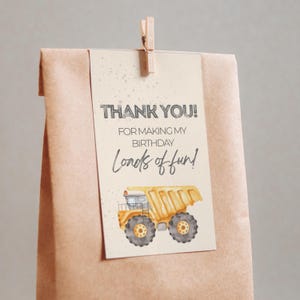 Könnte beinhalten: Eine braune Papiertüte mit einem Anhänger mit der Aufschrift "THANK YOU! FOR MAKING MY BIRTHDAY Loads of fun!". Der Anhänger zeigt eine Illustration eines gelben Muldenkippers.